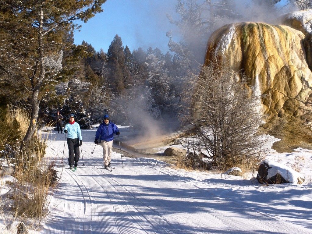 Two skiers cross-country ski past Orange Spring Mound on the Upper Terrace Ski Loop in Mammoth Hot Springs