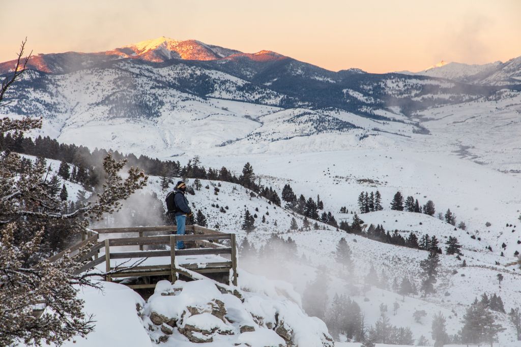 A lone tourist overlooks snow covered Mammoth Hot Springs terraces while the sun sets over the mountains