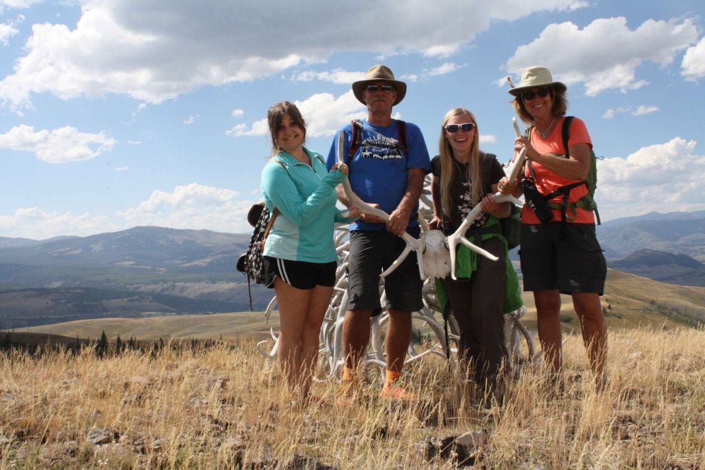 A group of four hikers stops along the trail to pose with elk antlers