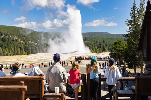 People on Old Faithful Inn deck watching Old Faithful erupt