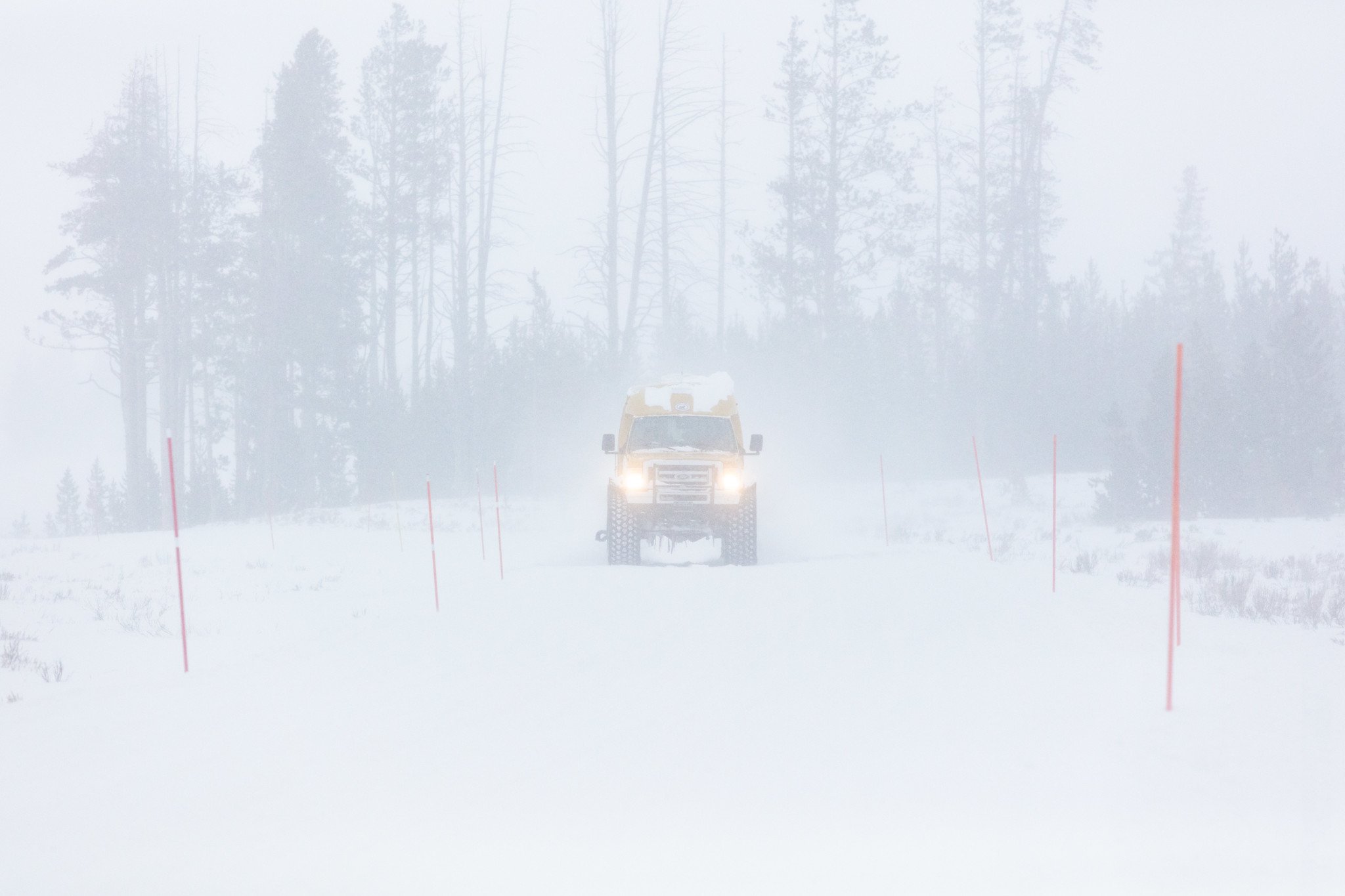 A snowcoach travels down the road during a winter storm