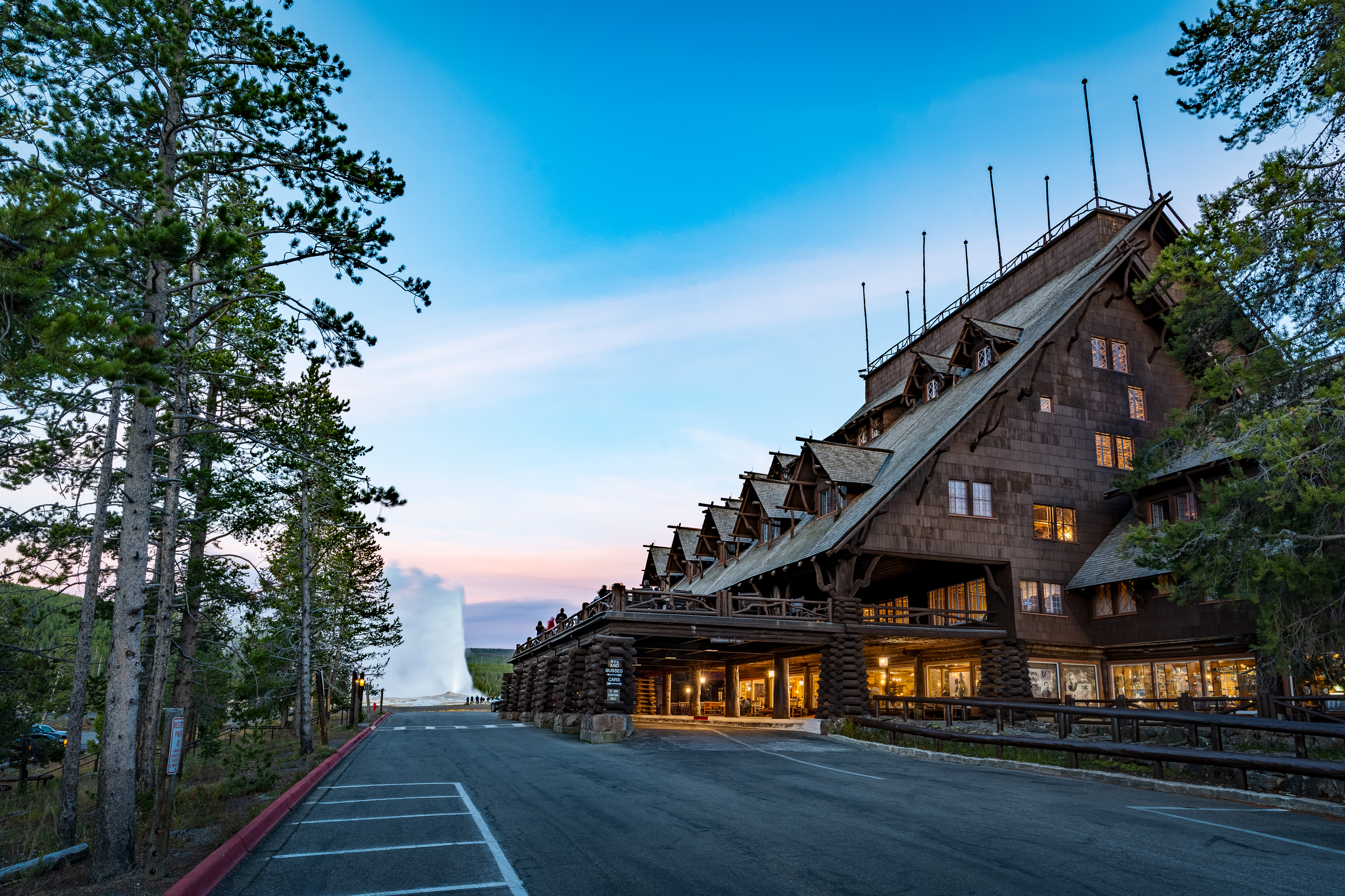 Old Faithful Inn at dusk with Old Faithful geyser erupting in the background