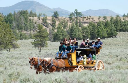 Passengers riding a stagecoach through a field with mountains in the background