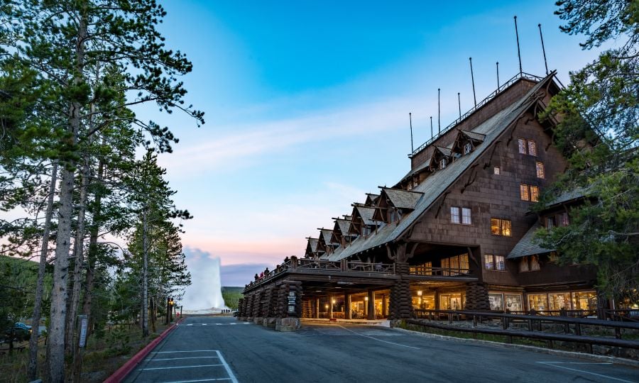 Old Faithful Inn at dusk with Old Faithful geyser erupting in the background