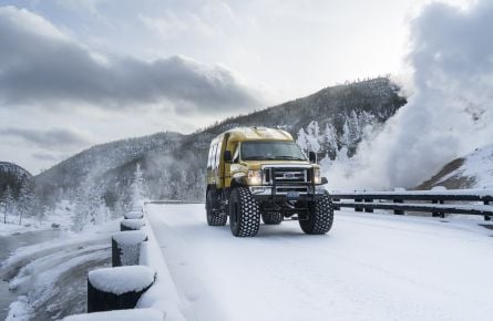 Snowcoach crossing snow-covered bridge with fumarole