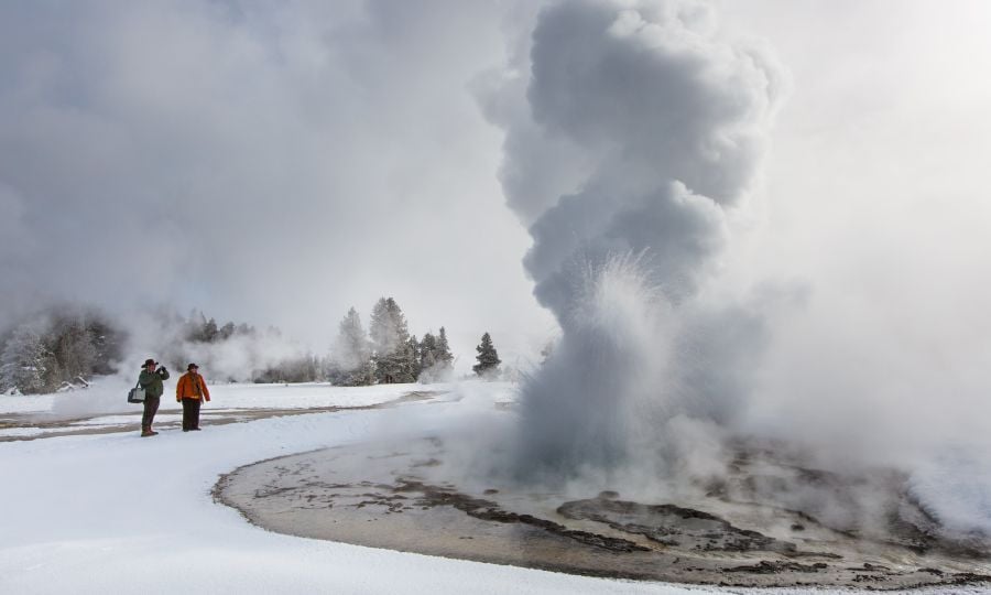 Two people watching a geyser in the snow