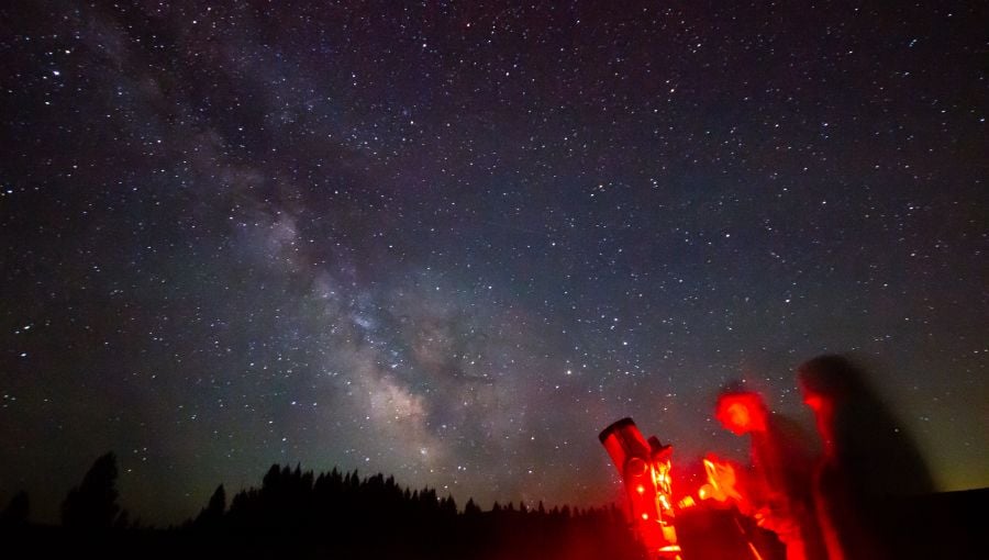 People standing next to a telescope viewing the Milky Way overhead
