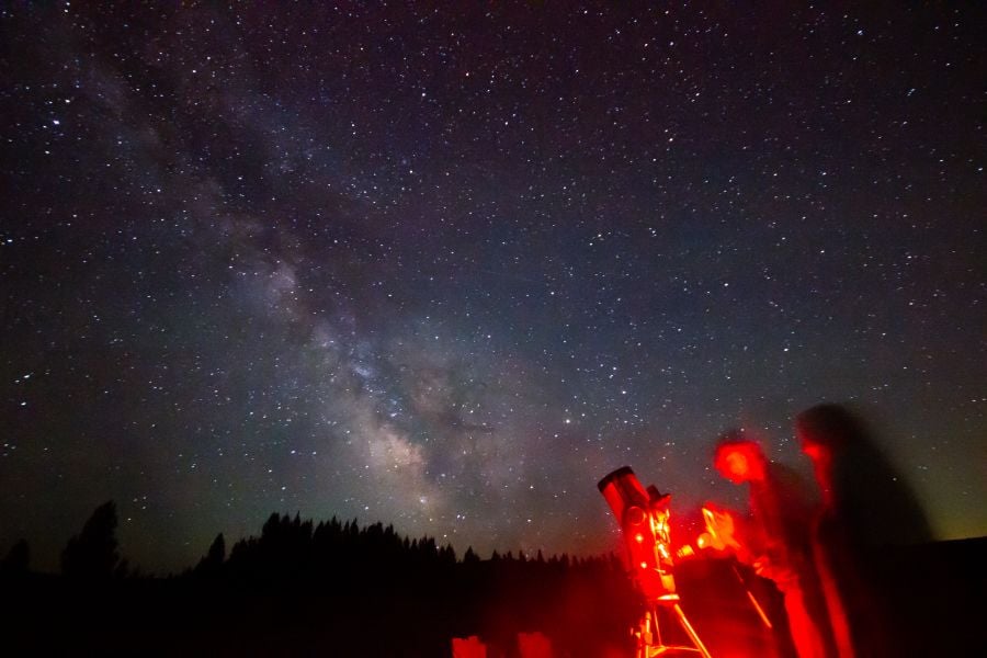 People standing next to a telescope viewing the Milky Way overhead