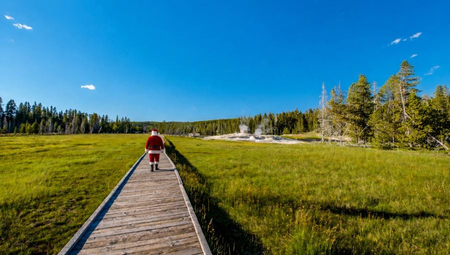 Santa walking on a boardwalk with geyser cones in the background